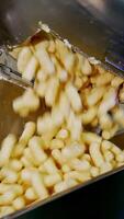 Sweet yellow crispy snacks falling on the conveyor line from opened metal tank. Maize sticks production process. Close up. Vertical video