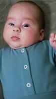 Quiet calm little boy lying on the bed and looking surprised into camera. Fine kid in blue clothes at grey backdrop. Close up. Vertical video