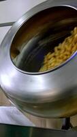 Two metal rotating tanks filled with sweet snacks. Corn sticks being covered with sugar syrup from a special disperse device. Vertical video