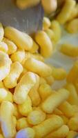 Light yellow crispy snacks falling on the conveyor belt. Corn sticks coated with sugar frosting close up. Vertical video
