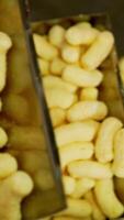 Production process of corn snacks at up-to-date food factory. Crunchy yellow sticks lifted by conveyor belt. Close up. Vertical video