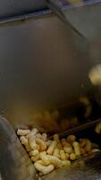 Sweet snacks made of maize are dropped into metal can. Manufacturing of vegetarian snacks at enterprise. Close up. Vertical video