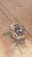New modern combine harvester mowing dry wheat in the field. Yellow agricultural machinery picking crops on the harvesting season. Vertical video