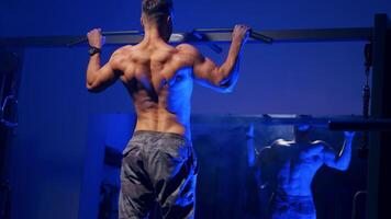 Man training on horizontal bar in gym. Back view portrait of young bodybuilder doing pull ups on the horizontal bar indoors video