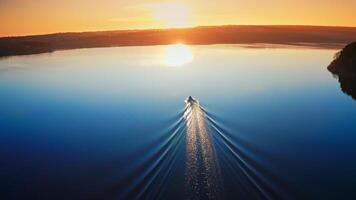 Aerial view of landscape during sunset. Camera follows the boat sailing on the river towards the sunset video