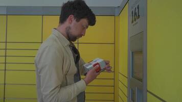 Male customer using self-service automated delivery terminal to send package or storage locker to drop off parcel. Postal automatic package pickup point man at operating screen holding phone and box. video