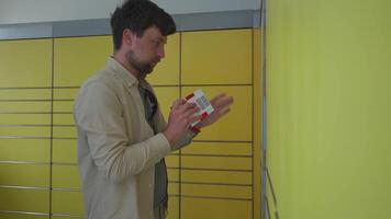 Man at packing station using screen and holding box for self shipment. Parcel pick-up point, parcel delivery, package delivery. Yellow self-service post terminal machine. Deposit parcel for storage. video