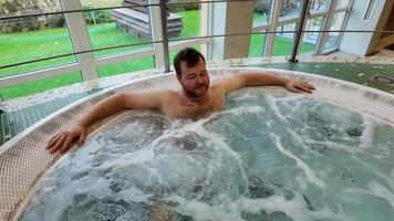 A Caucasian man relaxes in a bubbling jacuzzi spa, perfect for wellness retreats and leisure video