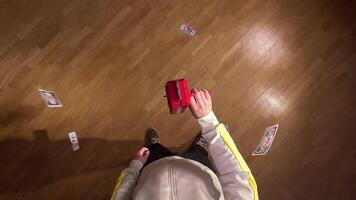 pov first person view Man is throwing fake dollar bills in the air using a red toy money gun, creating a playful scene of scattered cash on a wooden floor video