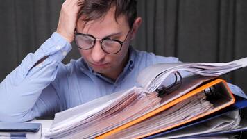 Young business man with eyeglasses having headache from too much paperwork and holding his head with hand while working in office video
