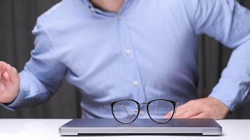 Office worker placing eyeglasses on closed laptop after finishing work on computer, ending workday, taking break from screen time, or protecting laptop screen. Businessman placing eyeglasses video