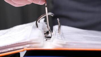 Close-up of an office worker's hand opening a ring binder mechanism to insert or archive documents, showcasing organization and paperwork in a professional setting video