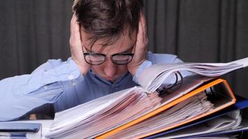 an office worker overloaded with work with documents is tired and clutches his head. The man is upset and clutches his head from the amount of work that has not been done. video