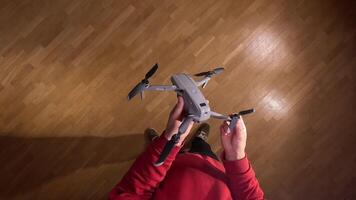 pov first person view man holds modern folding quadcopter drone in hands. Person mounting propellers on a gray foldable quadcopter drone, preparing it for flight, with a wooden floor in the background video