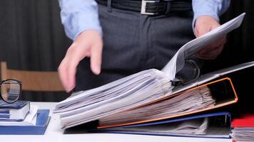 Busy office worker searches through a stack of files, highlighting the chaos of business paperwork. The image captures the stress of deadlines and the need for organization in the corporate world video