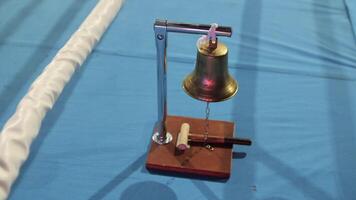 Boxing bell on a blue ring with mallet and white ropes, ready to signal rounds in a match, creating an intense and dynamic atmosphere video