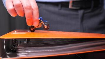 Businessman is holding a toy motorcycle above an orange folder, representing procrastination, work-life balance, and playful approach to business. Businessman playing with a toy motorcycle on a folder video
