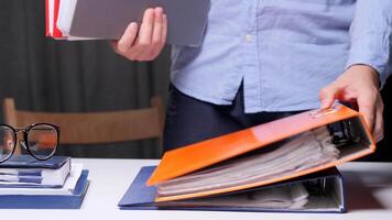 Office worker is managing paperwork, placing a red binder on a stack of colorful ring binders full of documents on a white desk video