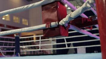 Close-up view of the corner padding and ropes of a boxing ring, highlighting the safety measures in place within a large, empty indoor arena, creating a sense of anticipation for an upcoming match video
