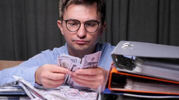office worker man Accountant carefully counting a stack of us dollar bills at his desk late at night, surrounded by financial documents and folders, diligently managing budget and expenses video
