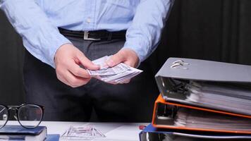 Businessman counting us dollars surrounded by office binders, showing finance and wealth themes. Capturing prosperity and growth in corporate world. A man in an office counts cash video