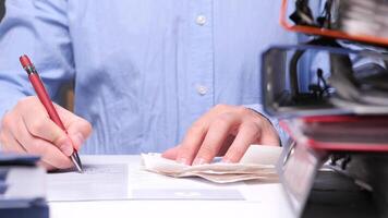 Man in a busy office fills out a tax form at his desk, surrounded by binders, showing responsibility and efficiency. His hand moves swiftly, capturing stress and pressure in a corporate job video