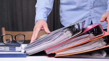 Office worker is putting a red ring binder on top of a stack of colorful ring binders full of paperwork, on a white desk. office worker puts a stack of folders with documents on his desk video