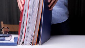 Office worker archives working documents in multi-colored folders and takes them to the archive from the desk. Office worker organizing paperwork on a desk in a busy workplace video