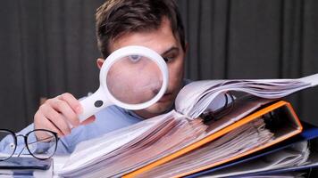 Accountant uses a magnifying glass to meticulously examine a large stack of financial documents, highlighting the pressures of meeting deadlines and the importance of accuracy in accounting video