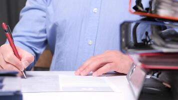 Office worker is diligently signing a document at a desk, with a stack of files subtly blurred in the foreground, emphasizing the focus on the task at hand. Office worker signing a document video