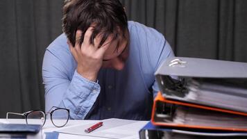 Office worker suffering from headache or stress, sitting at desk with stack of folders and documents, tired businessman having problems at work video