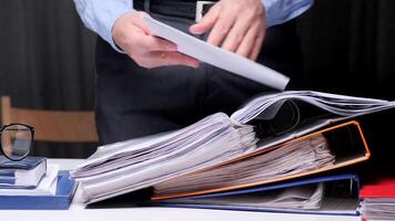 Office worker is searching through a large stack of binders and documents, indicating potential workload, deadline pressures, or administrative tasks video