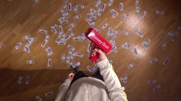 pov first person view Man in a stylish white sports jacket playfully holds a red money gun, making fake dollars rain down on a wooden parquet floor, evoking feelings of wealth and prosperity video