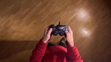 pov first person view Person wearing a red sweatshirt holding a generic wired controller, playing games at home. Gamer plays on console. Man quickly presses joystick buttons during game video