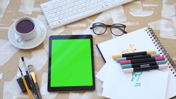 A tablet with a green screen on a table with a notebook, pens, and glasses, ideal for E-commerce video