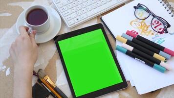 A woman is using a tablet with a green screen and a cup of coffee, ideal for digital content creation, remote work, and showcasing technology in a cozy, productive workspace video