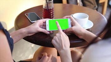 Two people sitting at a table with a green screen and tapping a mobile device, ideal for digital content creation, collaborative work, E-commerce, and creative projects video