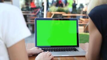 Two people sitting at a table with a laptop with a green screen, ideal for digital content creation, E-commerce, collaborative work, and showcasing technology for creative projects video
