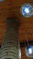 Modern ceiling with light lamp balls. Many round light balls hanging around brick column in the hall. Beautiful glass bulbs on brown background. Vertical video
