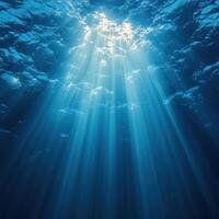 Beneath surface, rays of light pierce through tranquil blue waters, creating serene underwater scene filled with calmness and beauty photo