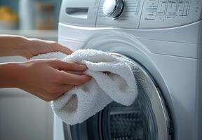person is placing white towel into washing machine, demonstrating laundry care and household chores. scene conveys sense of cleanliness and organization photo