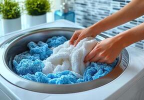 Washing colorful towels in modern washing machine, hands gently placing white and blue towels inside. scene conveys sense of cleanliness and freshness photo