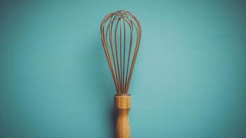 kitchen whisk with wooden handle against turquoise background, perfect for mixing and blending ingredients. This essential tool adds touch of elegance to any culinary space photo