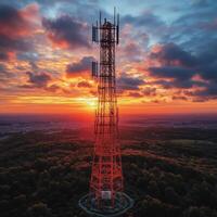 telecommunications network tower stands tall against vibrant sunset, surrounded by lush greenery. sky is painted with dramatic clouds, creating stunning backdrop photo