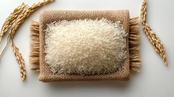 pile of white rice grains is centered on burlap sack, surrounded by rice stalks, showcasing natural beauty and simplicity of this staple food photo