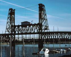 Serene Lakeside Scene Featuring a Boat Under a Cloudy Sky Near a Girder Bridge photo