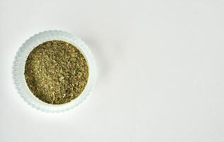 Dry ocha or green tea organic beverage leaves in round glass bowl container isolated on horizontal copy spaced white background. photo