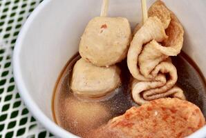 Oden fish cake sticks with soup in white paper bowl isolated on horizontal white metal table surface background. photo