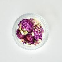 Dried globe amaranth or gomphrena globosa flowers for tea ingredients in round glass bowl container isolated on square white background from above view angle. photo