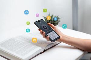 Hand holding smartphone above open book, using voice-to-text app for learning, representing audio search and text-to-speech technology, with floating icons for study and communication concepts photo